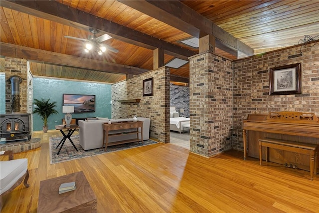 1369 Old Pulaski Rd, Neshannock Twp, PA 16105 - living room featuring a wood stove, wooden ceiling with exposed beams, wood finished floors, ceiling fan, and brick wall