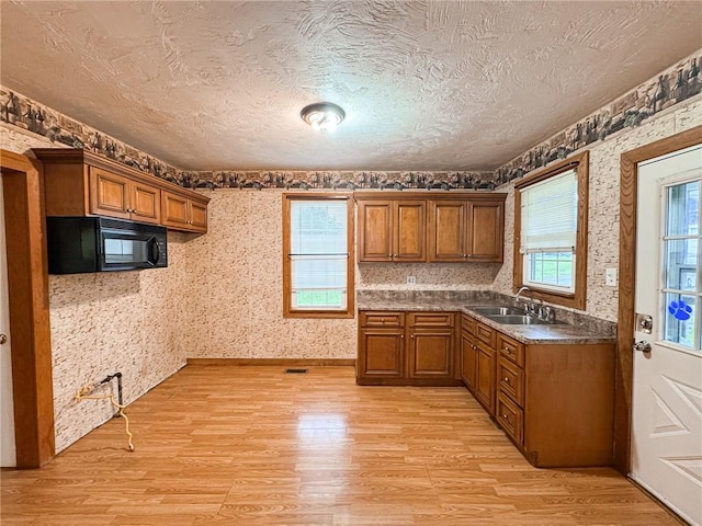 2701 Lafayette St, Mckeesport, PA 15132 - kitchen with black microwave, brown cabinetry, light wood-style flooring, a textured ceiling, and a sink