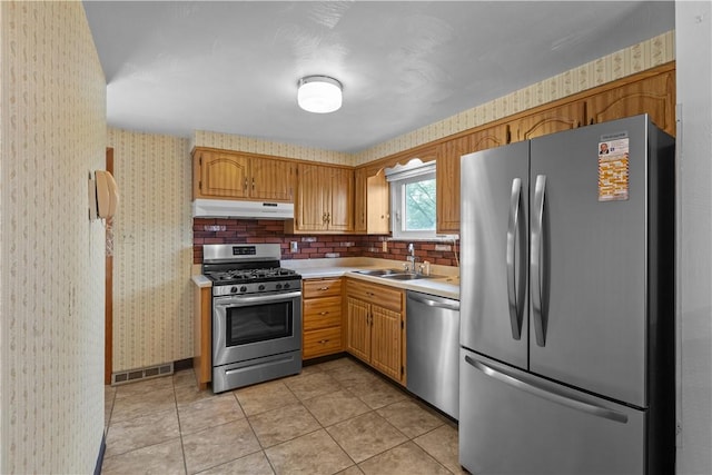 719 12th St, Pitcairn, PA 15140 - kitchen featuring appliances with stainless steel finishes, a sink, under cabinet range hood, wallpapered walls, and light countertops