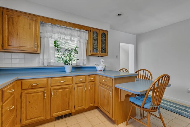 332 Division Ln, Vanport, PA 15009 - kitchen with a kitchen breakfast bar, a peninsula, brown cabinetry, glass insert cabinets, and light tile patterned floors