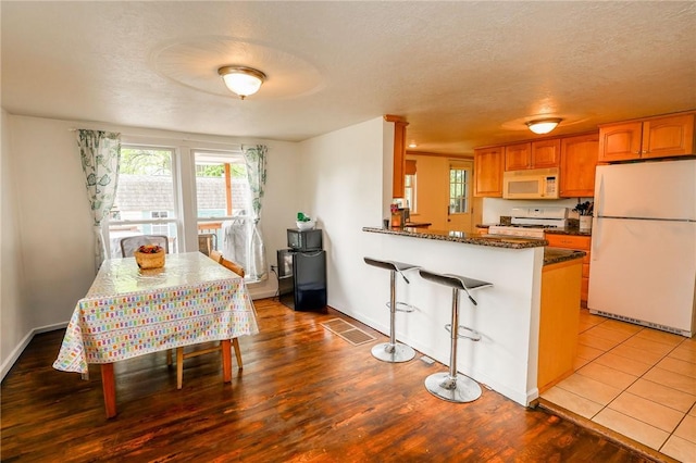 343 Whitestown Rd, Twp Of But Nw, PA 16001 - kitchen featuring white appliances, wood finished floors, brown cabinets, a kitchen bar, and a textured ceiling