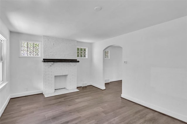 8536 Pershing St, Penn Hills, PA 15235 - unfurnished living room featuring arched walkways, a brick fireplace, healthy amount of natural light, and wood finished floors