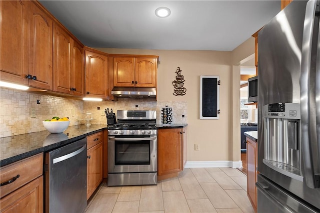 1299 Oakridge Rd, South Fayette, PA 15057 - kitchen with stainless steel appliances, under cabinet range hood, brown cabinets, light tile patterned floors, and tasteful backsplash