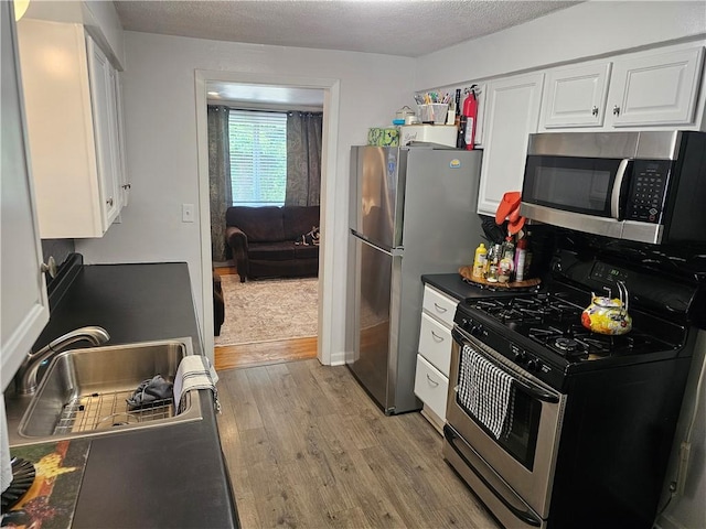 1099 Vine St, Coraopolis, PA 15108 - kitchen featuring stainless steel appliances, light wood finished floors, white cabinetry, a sink, and a textured ceiling