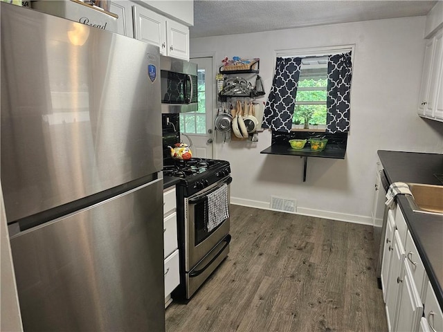 1099 Vine St, Coraopolis, PA 15108 - kitchen featuring appliances with stainless steel finishes, dark countertops, dark wood-type flooring, white cabinets, and a textured ceiling
