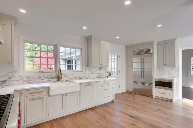 129 S Dr, Fox Chapel, PA 15238 - kitchen featuring appliances with stainless steel finishes, a sink, tasteful backsplash, light wood finished floors, and light stone countertops