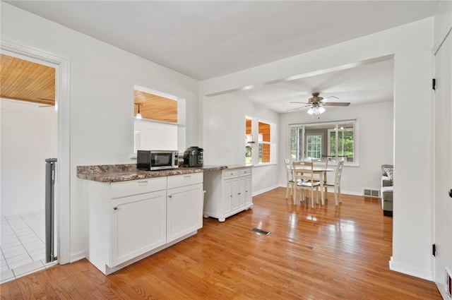 3702 School Rd, Murrysville, PA 15668 - kitchen with stainless steel microwave, light wood finished floors, white cabinetry, a ceiling fan, and dark stone countertops
