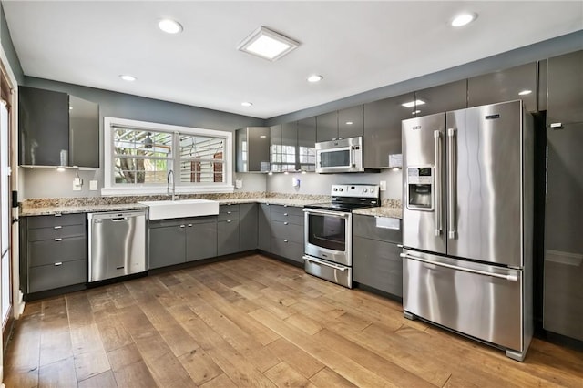 4825 Hatfield St, Lawrenceville, PA 15201 - kitchen featuring stainless steel appliances, a sink, gray cabinetry, light wood-type flooring, and light stone countertops
