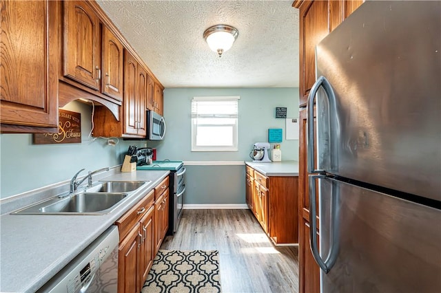 1941 Ivanhoe Dr, North Huntingdon, PA 15642 - kitchen with stainless steel appliances, a sink, light wood-style floors, brown cabinetry, and a textured ceiling