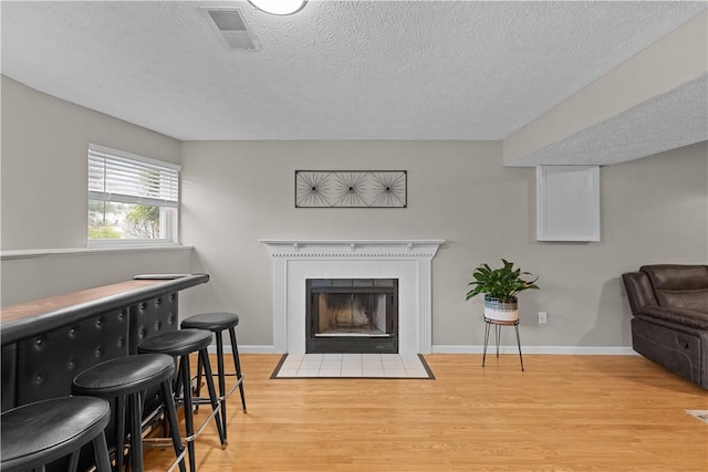 509 Cresthaven Dr, Plum Boro, PA 15239 - living area featuring light wood-style flooring, a textured ceiling, a tile fireplace, baseboards, and a bar