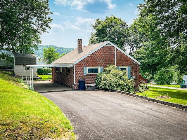 145 7th St, E Butler Boro, PA 16029 - view of property exterior featuring a carport, brick siding, asphalt driveway, a yard, and a chimney