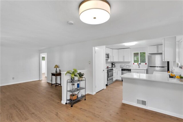 9830 Don Dr, North Huntingdon, PA 15642 - kitchen featuring appliances with stainless steel finishes, light countertops, light wood-style floors, a peninsula, and white cabinets