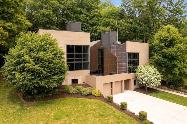 340 Lakewood Rd, Unity Twp, PA 15601 - rear view of property with concrete driveway, an attached garage, a chimney, stucco siding, and a lawn