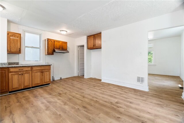 1567 Princeton Blvd, Wilkinsburg, PA 15221 - kitchen with brown cabinetry, under cabinet range hood, light wood-type flooring, stone countertops, and baseboards