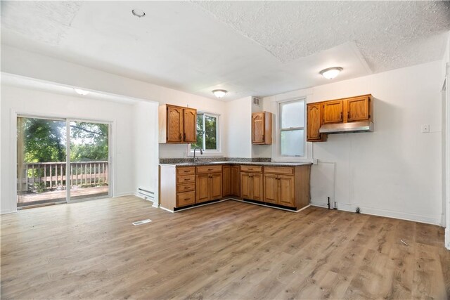 1567 Princeton Blvd, Wilkinsburg, PA 15221 - kitchen featuring brown cabinets, under cabinet range hood, a baseboard radiator, light wood finished floors, and a textured ceiling