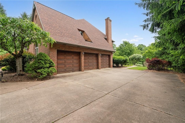 26 Indian Fields Trl, Lower Burrell, PA 15068 - view of side of home with a garage, a chimney, a shingled roof, concrete driveway, and brick siding