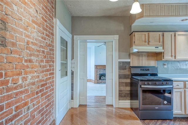 1457 Orator St, Crafton Heights, PA 15204 - kitchen with stainless steel range with gas stovetop, under cabinet range hood, light wood finished floors, light brown cabinetry, and a brick fireplace