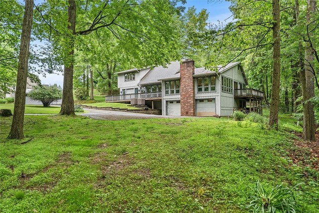 124 Oak Ln, Adams Twp, PA 16046 - back of property featuring an attached garage, a chimney, a deck, driveway, and a yard