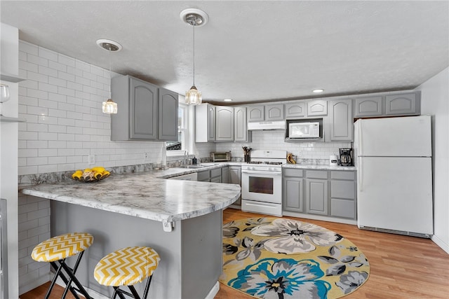 205 Cottage St, Neville Twp, PA 15225 - kitchen featuring white appliances, gray cabinetry, a peninsula, under cabinet range hood, and a breakfast bar