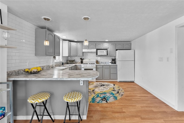 205 Cottage St, Neville Twp, PA 15225 - kitchen featuring white appliances, gray cabinets, a peninsula, under cabinet range hood, and a breakfast bar area