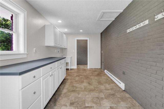 626 Solomon Temple Rd, Unity Twp, PA 15650 - kitchen with baseboard heating, brick wall, an accent wall, white cabinetry, and stone finish floors