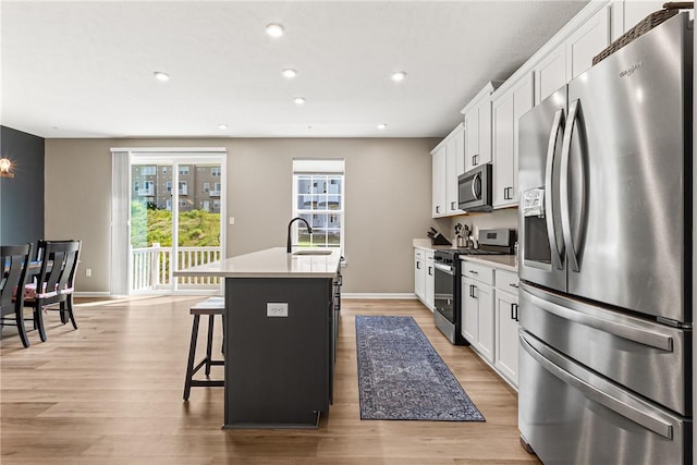 136 Sweetwater Dr, Moon/Crescent Twp, PA 15108 - kitchen featuring stainless steel appliances, an island with sink, a kitchen breakfast bar, white cabinetry, and light wood-style flooring