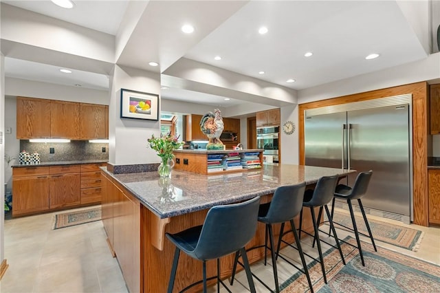337 Fox Chapel Rd, Fox Chapel, PA 15238 - kitchen with appliances with stainless steel finishes, brown cabinetry, a spacious island, decorative backsplash, and recessed lighting