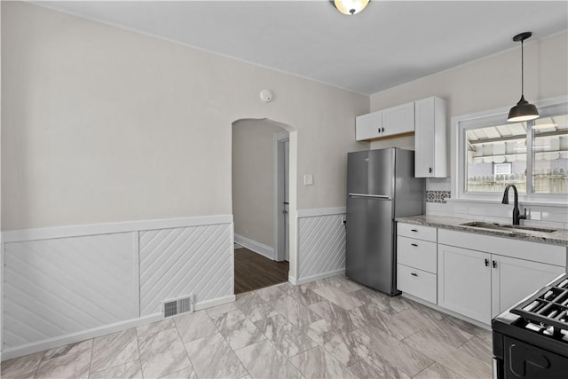 4506 Bowes Ave, West Mifflin, PA 15122 - kitchen featuring freestanding refrigerator, wainscoting, arched walkways, light stone counters, and white cabinetry
