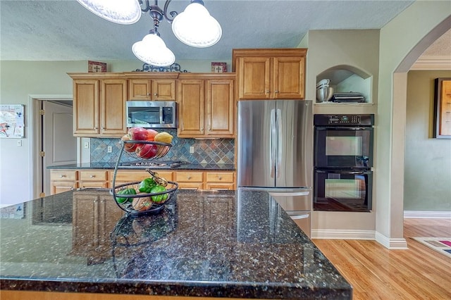 2023 Sterling Dr, South Fayette, PA 15057 - kitchen featuring appliances with stainless steel finishes, arched walkways, light wood-style flooring, backsplash, and a textured ceiling