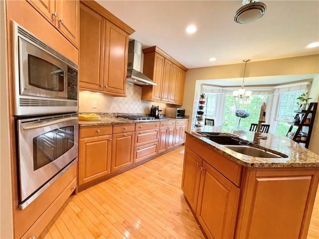 518 Farndale Rd, Ohara, PA 15238 - kitchen featuring appliances with stainless steel finishes, wall chimney exhaust hood, light wood finished floors, a kitchen island with sink, and decorative backsplash
