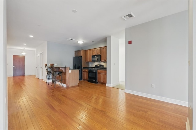 151 Fort Pitt Blvd Unit 1403, Downtown Pgh, PA 15222 - kitchen with black appliances, a breakfast bar, dark countertops, light wood-style flooring, and brown cabinetry