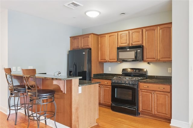 151 Fort Pitt Blvd Unit 1403, Downtown Pgh, PA 15222 - kitchen featuring black appliances, a kitchen bar, light wood-style floors, and dark stone counters