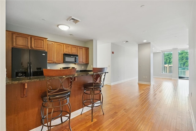 151 Fort Pitt Blvd Unit 1403, Downtown Pgh, PA 15222 - kitchen with black appliances, a kitchen bar, brown cabinetry, light wood finished floors, and dark stone counters