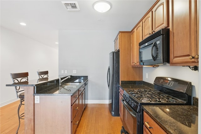151 Fort Pitt Blvd Unit 1403, Downtown Pgh, PA 15222 - kitchen with black appliances, a kitchen bar, light wood-style flooring, a peninsula, and dark stone counters
