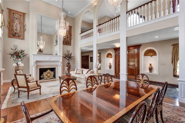 7023 Fair Oaks Dr, Export, PA 15632 - dining area with wood finished floors, a towering ceiling, a chandelier, a fireplace with raised hearth, and decorative columns