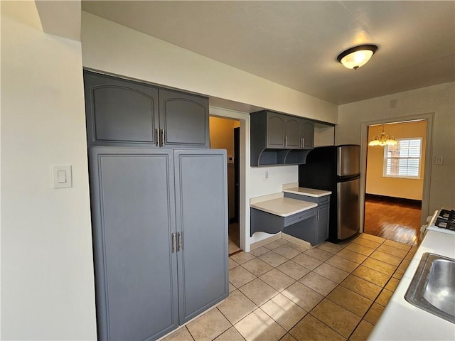 619 Ridge Ave, New Kensington, PA 15068 - kitchen featuring gray cabinetry, freestanding refrigerator, light tile patterned flooring, light countertops, and a chandelier