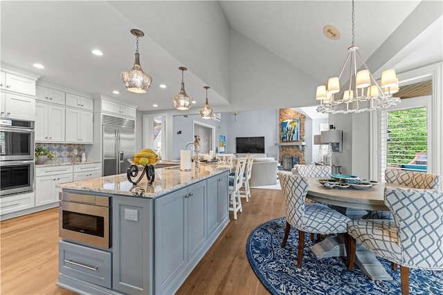 1055 Saint Mellion Dr, Collier Twp, PA 15142 - kitchen featuring appliances with stainless steel finishes, open floor plan, white cabinets, a stone fireplace, and light wood-type flooring