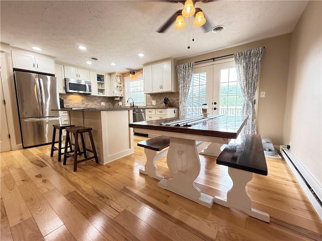 84 Williamson Rd, Hempfield Twp Mer, PA 16125 - kitchen with stainless steel appliances, a textured ceiling, baseboard heating, light wood-style floors, and a kitchen breakfast bar