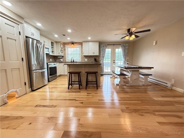 84 Williamson Rd, Hempfield Twp Mer, PA 16125 - kitchen featuring stainless steel appliances, a baseboard radiator, a textured ceiling, light wood-style flooring, and a breakfast bar area