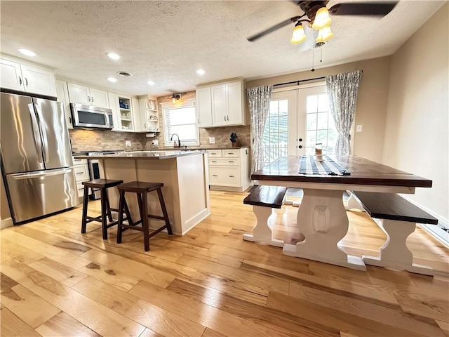 84 Williamson Rd, Hempfield Twp Mer, PA 16125 - kitchen with appliances with stainless steel finishes, a textured ceiling, light wood-style floors, decorative backsplash, and a kitchen breakfast bar