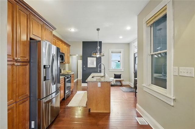 2315 Jane St, South Side, PA 15203 - kitchen with appliances with stainless steel finishes, brown cabinets, a kitchen island with sink, light stone countertops, and dark wood finished floors
