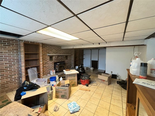 105 Fern Way, Glassport, PA 15045 - finished basement featuring a wood stove, tile patterned floors, a paneled ceiling, and brick wall
