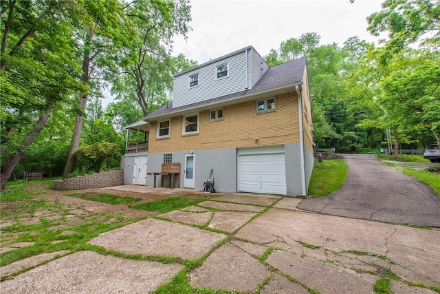 670 Lougeay Rd, Penn Hills, PA 15235 - back of house featuring a garage, driveway, brick siding, and view of wooded area