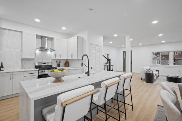 2356 Pittock St, Squirrel Hill, PA 15217 - kitchen with wall chimney range hood, stainless steel gas stove, a kitchen breakfast bar, white cabinets, and recessed lighting