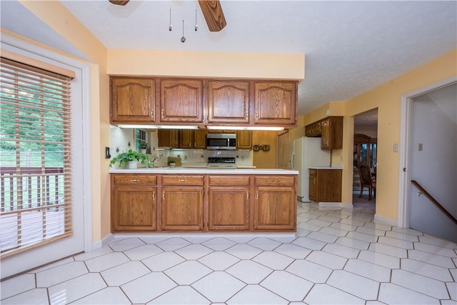 221 William Dr, North Strabane, PA 15317 - kitchen with stainless steel microwave, freestanding refrigerator, a peninsula, brown cabinetry, and light countertops