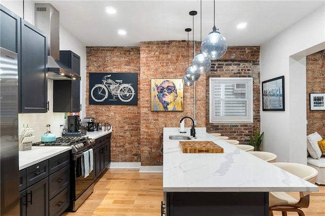 161 Morewood, Oakland, PA 15213 - kitchen with stainless steel gas range, brick wall, wall chimney exhaust hood, light wood-style flooring, and a breakfast bar