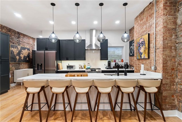 161 Morewood, Oakland, PA 15213 - kitchen featuring wall chimney range hood, stainless steel appliances, a kitchen bar, light wood finished floors, and brick wall