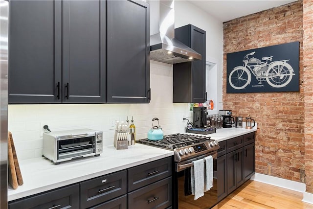 161 Morewood, Oakland, PA 15213 - kitchen featuring stainless steel range with gas cooktop, wall chimney exhaust hood, light wood finished floors, tasteful backsplash, and brick wall