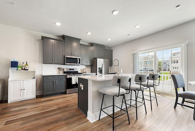 1408 Commons Ln, South Fayette, PA 15017 - kitchen featuring appliances with stainless steel finishes, light wood-type flooring, an island with sink, a breakfast bar, and light countertops