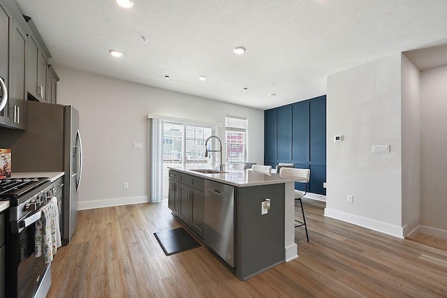 1408 Commons Ln, South Fayette, PA 15017 - kitchen featuring appliances with stainless steel finishes, wood finished floors, a kitchen island with sink, a kitchen bar, and light countertops